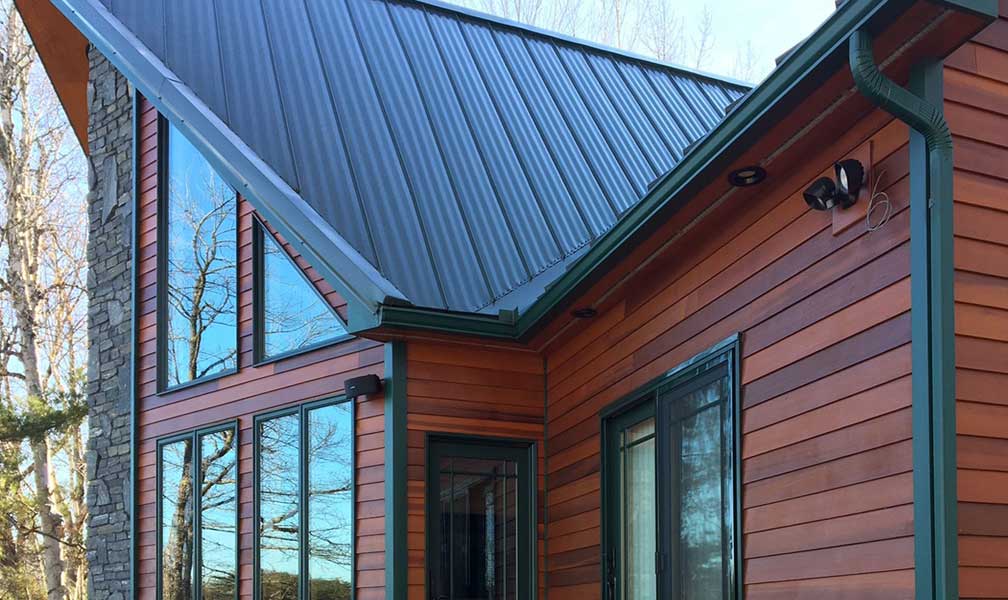 Earthadelic offers new gutter installations in a variety of colors to match any style. These green gutters on a log cabin provide a rustic look.